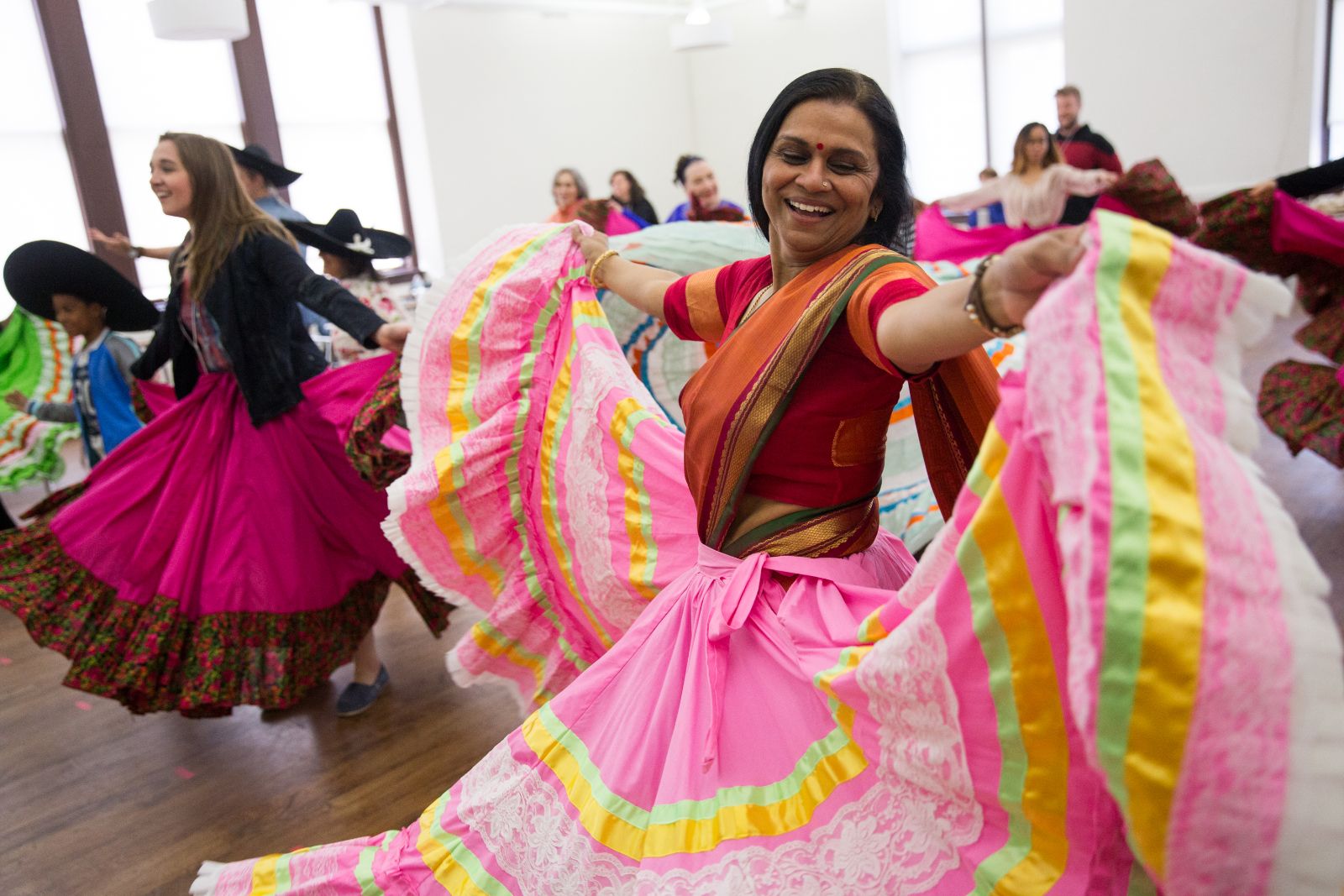 A smiling dancer wearing a large, pink ruffled skirt holds the folds of the skir